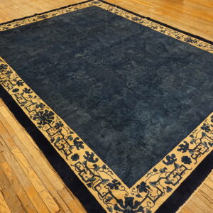 Rectangular indigo rug with a gold floral-patterned border shown on worn hardwood flooring.