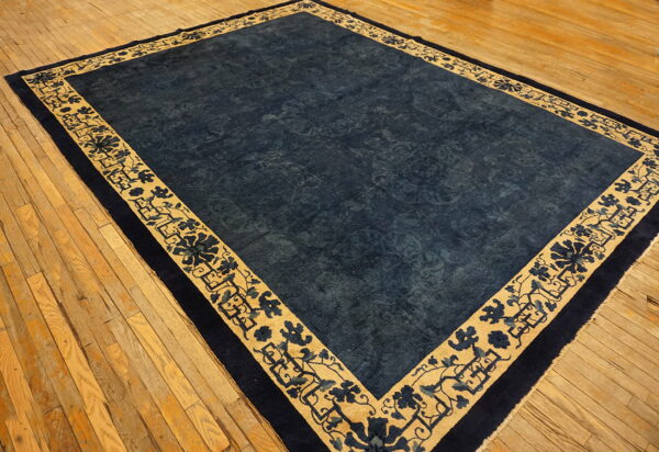 Rectangular indigo rug with a gold floral-patterned border shown on worn hardwood flooring.