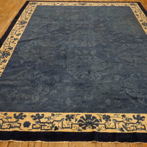 Navy blue rug featuring subtle medallions and a wide cream border with dark floral patterns rests on wood planks.