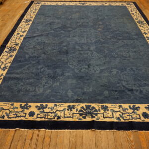 Dark blue rug with faded floral patterns and a wide beige and blue patterned border on wood floorboards.