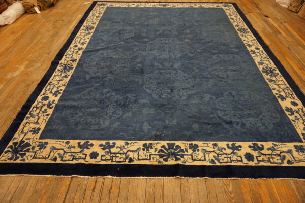 Dark blue rug with faded floral patterns and a wide beige and blue patterned border on wood floorboards.