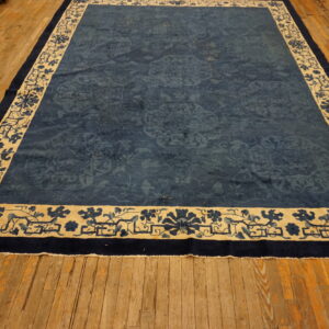 A large deep blue rug with a beige floral border rests on wide distressed hardwood flooring.