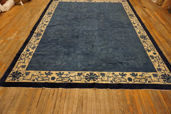 A large deep blue rug with a beige floral border rests on wide distressed hardwood flooring.