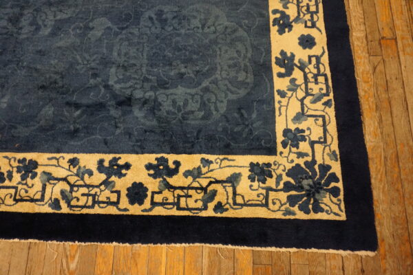 Dark blue high-pile rug with subtle tone-on-tone field and wide tan floral border on wood floors.