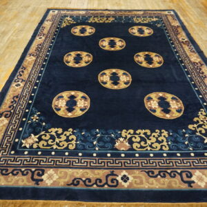 Navy blue rug featuring tan medallions and patterned borders displayed on worn, light wood flooring.