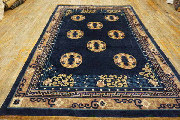 Navy blue rug featuring tan medallions and patterned borders displayed on worn, light wood flooring.