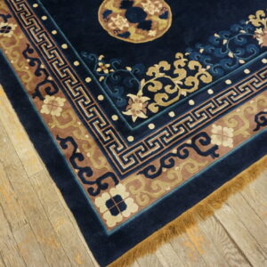 Navy blue rug with carved borders of tan, mauve, and light blue resting on distressed wood floor.