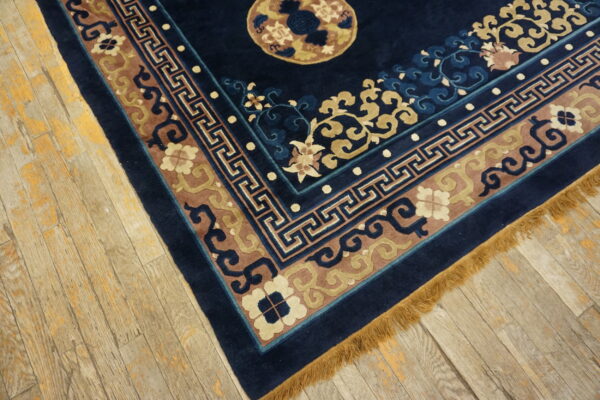 Navy blue rug with carved borders of tan, mauve, and light blue resting on distressed wood floor.