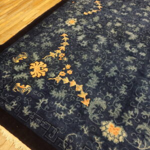 Ornate dark blue rug with gold and light blue botanical designs rests on golden wood floors.