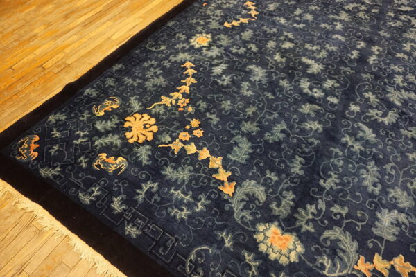 Ornate dark blue rug with gold and light blue botanical designs rests on golden wood floors.