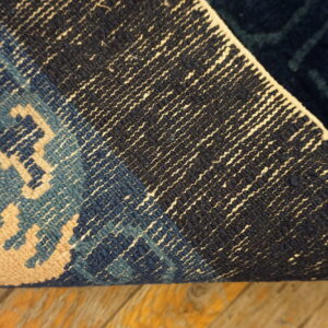 The back of a blue, navy, and cream patterned rug curled on distressed wooden flooring.