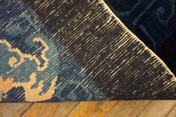 The back of a blue, navy, and cream patterned rug curled on distressed wooden flooring.