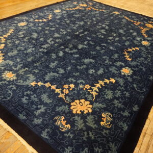 Dark blue rug with contrasting orange and lighter blue floral motifs rests on plank wood flooring.