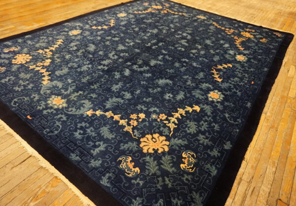 Dark blue rug with contrasting orange and lighter blue floral motifs rests on plank wood flooring.