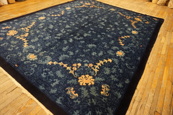 Large dark blue rug with intricate pale blue and peach floral patterns on a warm plank wood floor.