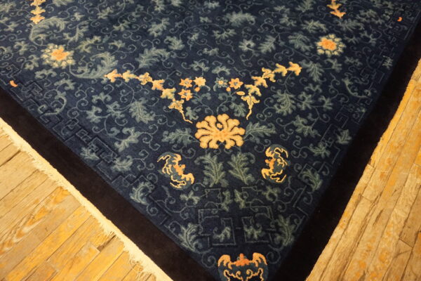 Navy blue rug features intricate floral and vine patterns in peach and pale green on hardwood floors.