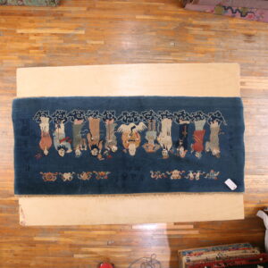 Overhead view of a deep blue rug patterned with figures and a crane on a light wood board.