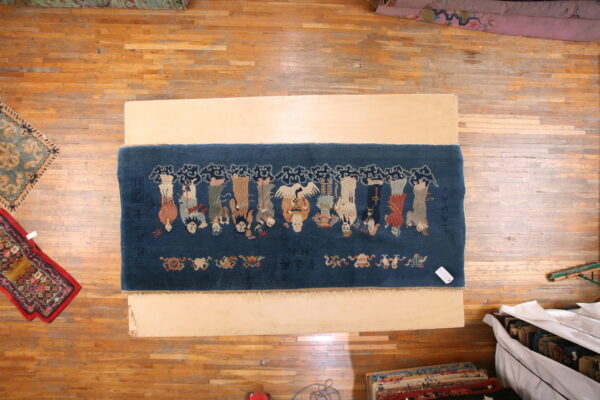 Overhead view of a deep blue rug patterned with figures and a crane on a light wood board.