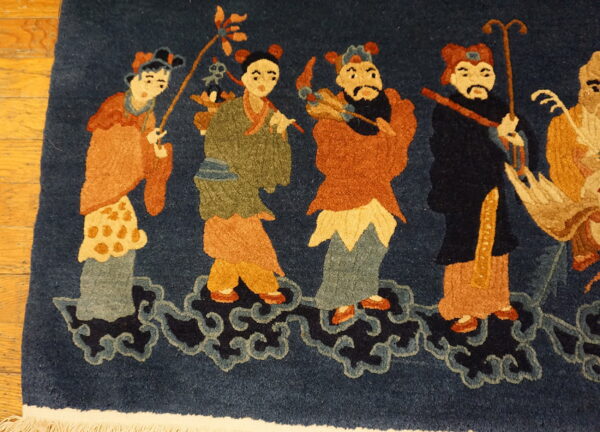 Deep blue high-pile rug with rust, gold, and sage figures standing on stylized navy cloud motifs.