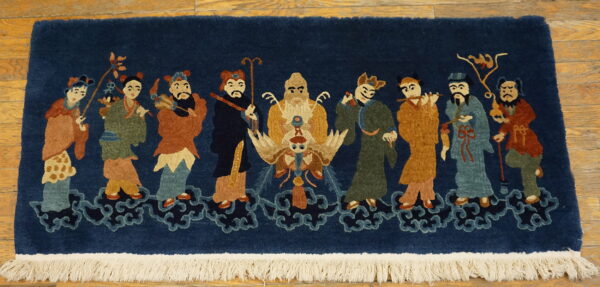High-pile navy rug with a scene of nine colorful figures on clouds, finished with white fringe on wood floor.