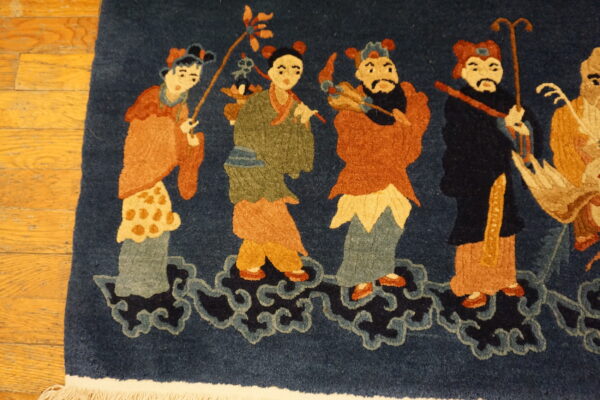 Detailed view of a blue rug with a figural pattern in rust and green, resting on honey-colored wood floors.