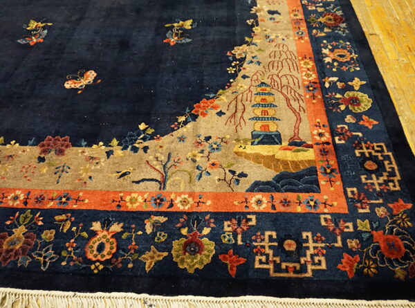 Detailed navy rug with a pagoda and landscape scene, bordered by rust-orange and floral geometric patterns.