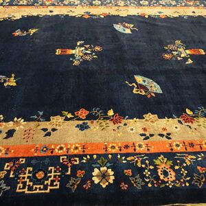 Navy blue rug with scattered floral and fan designs and elaborate tan, orange, and floral borders.