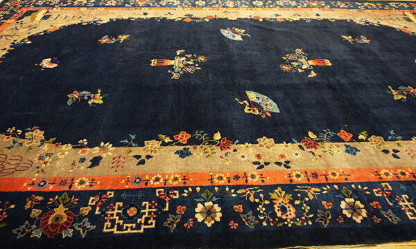 Navy blue rug with scattered floral and fan designs and elaborate tan, orange, and floral borders.