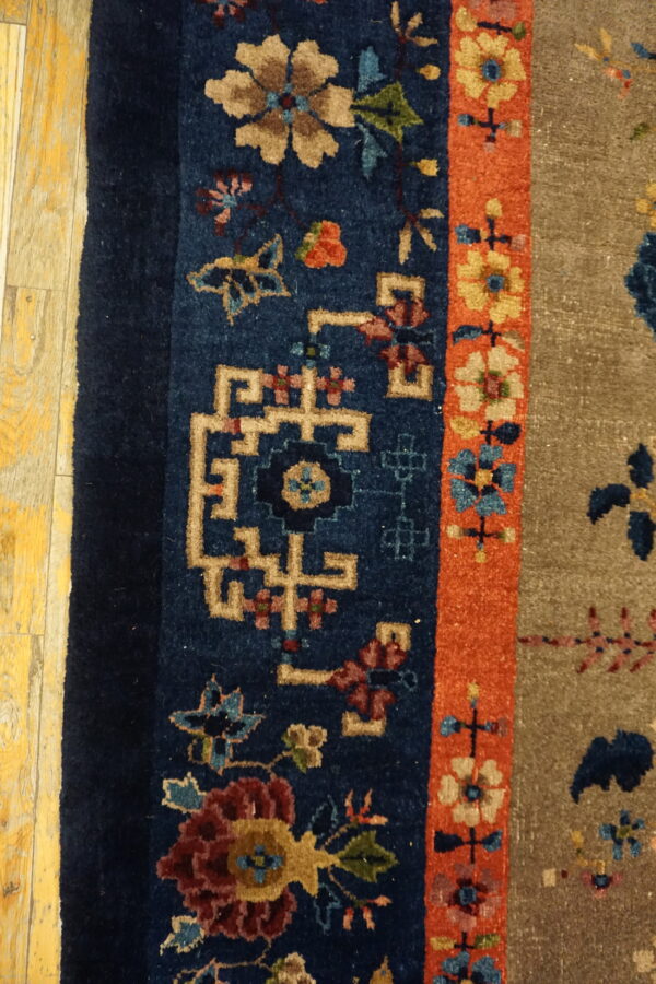 Textured, detailed rug featuring tan, blue, and orange floral borders next to worn yellow wood flooring.
