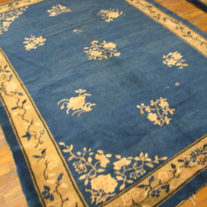 Navy blue rug featuring a scattered floral pattern and a wide tan border on light wood flooring.