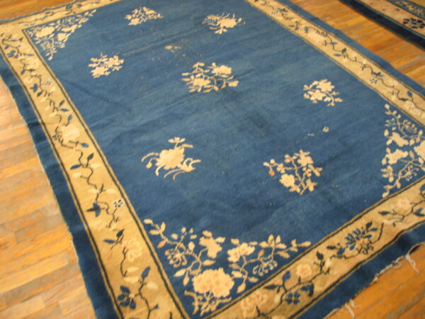 Navy blue rug featuring a scattered floral pattern and a wide tan border on light wood flooring.