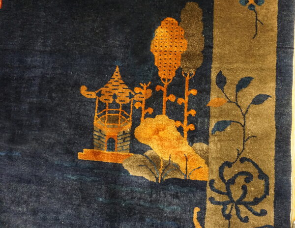 Dark blue rug detail featuring an orange pagoda, brown trees, and a vertical khaki-colored border design.