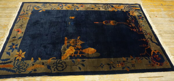 Plush navy blue rug with a taupe border and gold scenic patterns on light wood flooring.