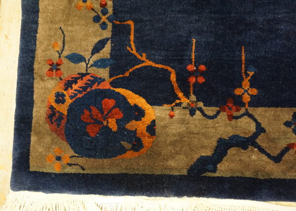 Navy blue rug corner featuring tan accents and bold orange, blue, and red botanical motifs.