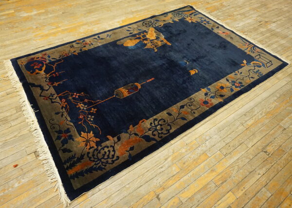 Navy rug with orange and blue floral motifs bordering the field on distressed wood flooring.