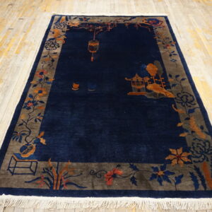 Deep blue rug with a scenic border in gray and terracotta rests on pale, worn wooden flooring.