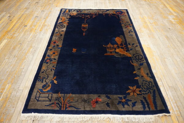 Deep blue rug with a scenic border in gray and terracotta rests on pale, worn wooden flooring.