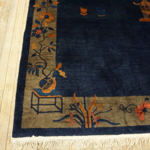 A deep navy rug with a broad brown border featuring orange and blue floral patterns rests on light wood floors.