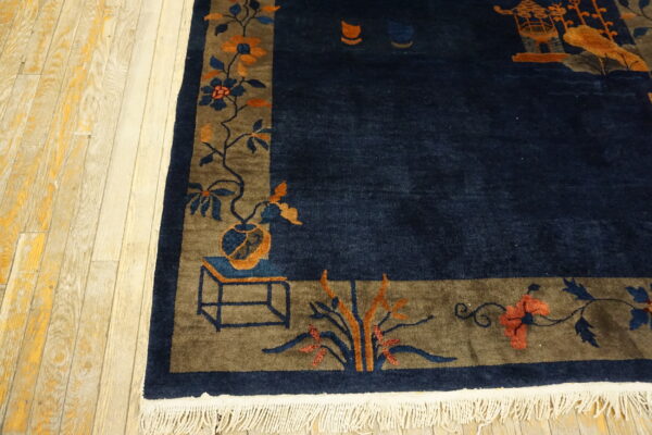 A deep navy rug with a broad brown border featuring orange and blue floral patterns rests on light wood floors.