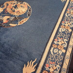 Close-up of a deep blue rug showing a tan dragon motif and complex floral and key pattern border.