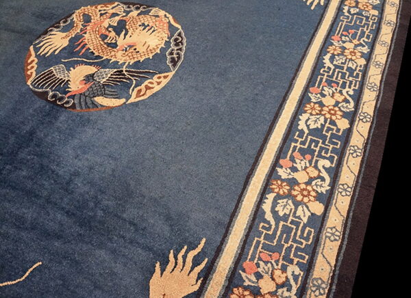 Close-up of a deep blue rug showing a tan dragon motif and complex floral and key pattern border.