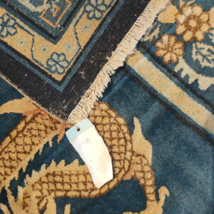 Overlapping blue and gold patterned rugs, one showing fringe and a price tag partially covering a dragon motif.