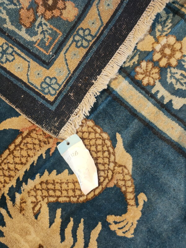 Overlapping blue and gold patterned rugs, one showing fringe and a price tag partially covering a dragon motif.