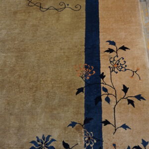 Tan rug with dark blue and orange floral vines and a vertical border stripe on distressed wood floorboards.