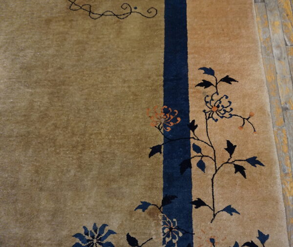 Tan rug with dark blue and orange floral vines and a vertical border stripe on distressed wood floorboards.