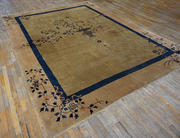 Muted gold rug with a central vase motif and blue floral borders rests on weathered wood planks.
