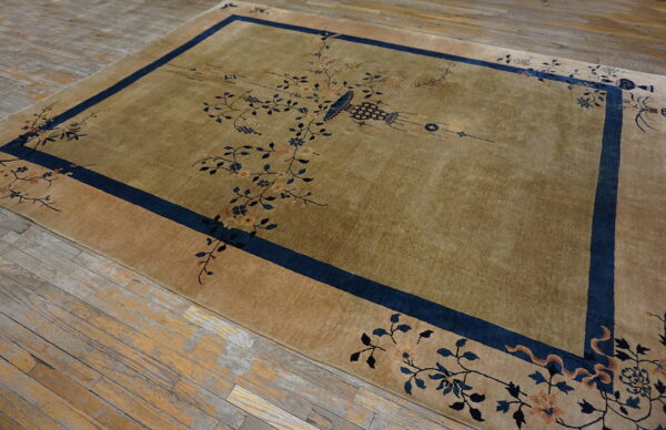 Lustrous olive rug with a blue border and delicate floral motifs covers rustic wood flooring.