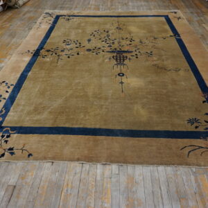An olive and tan rug featuring a central vase and blue floral motifs rests on worn wooden planks.