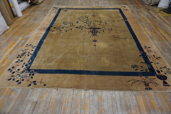 An olive and tan rug featuring a central vase and blue floral motifs rests on worn wooden planks.