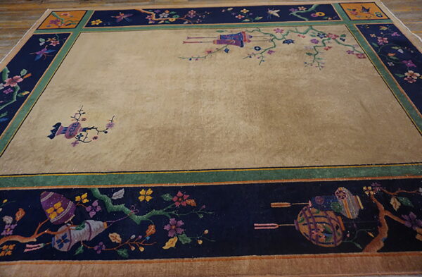 A large rug with a tan field and a wide navy border featuring colorful floral and lantern patterns.
